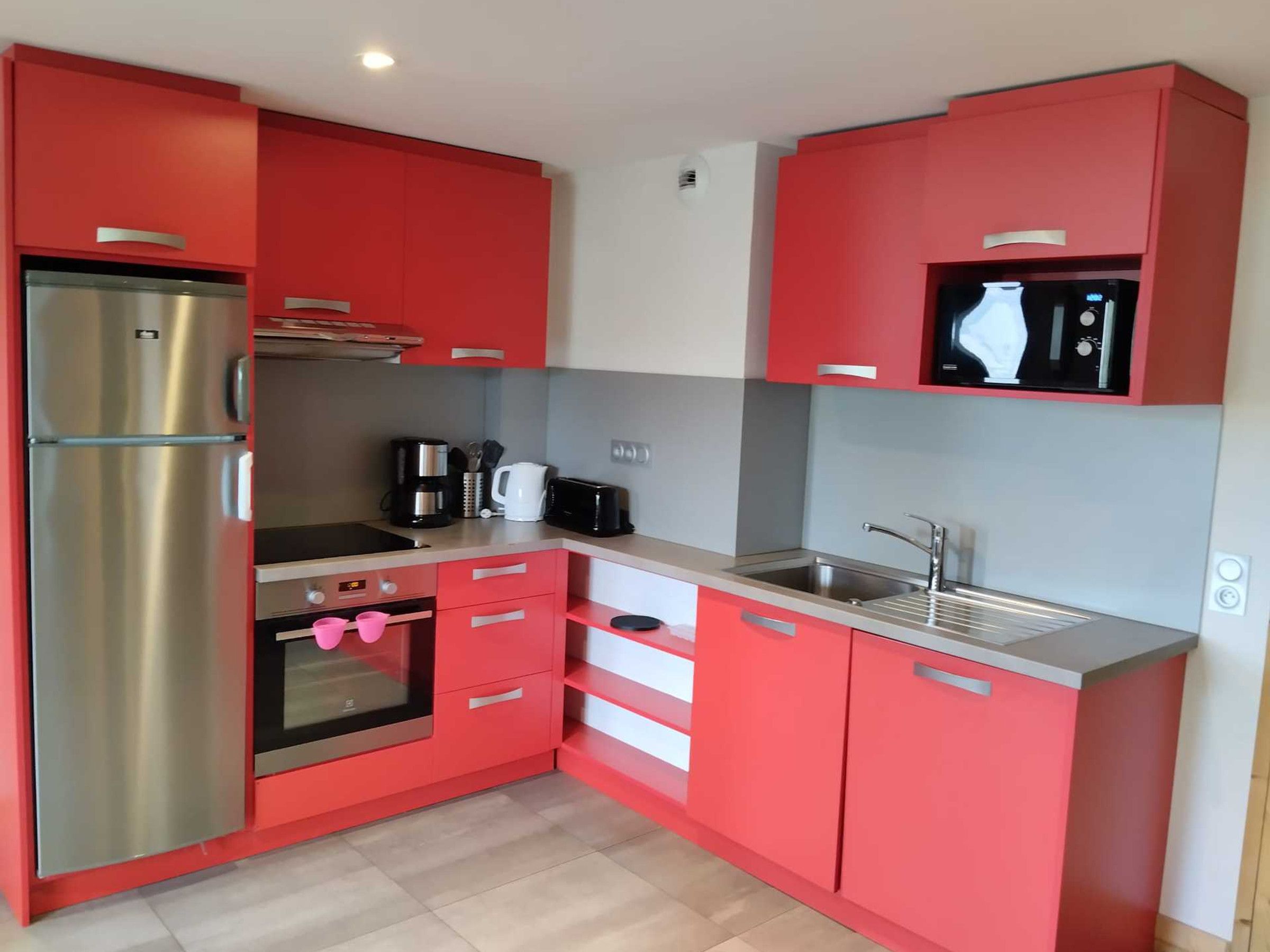 A compact kitchen with red cabinets, a stainless steel refrigerator, a microwave, a coffee maker, and a sink.