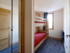 A small, compact room with a bunk bed, a wooden wardrobe, and a window providing natural light.