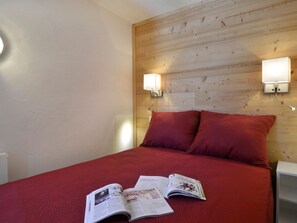 A room with a wooden headboard, two wall-mounted reading lights, a red bedspread, and a magazine on the bed.