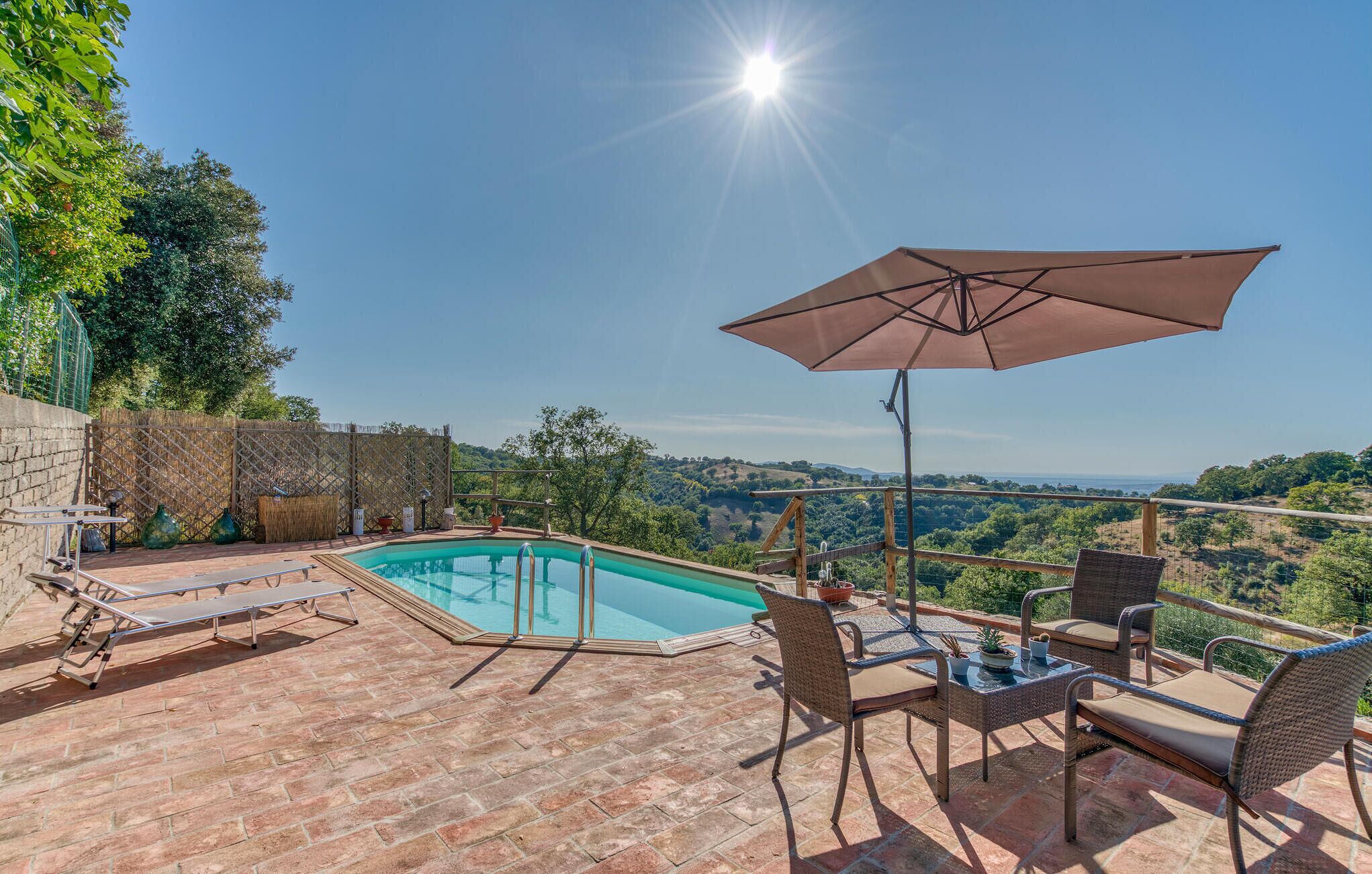 A poolside area with a view of the countryside, a covered seating area, and a brick patio.