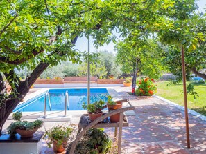 Zona de piscina con vista despejada, rodeada de plantas en macetas y un camino de ladrillo.