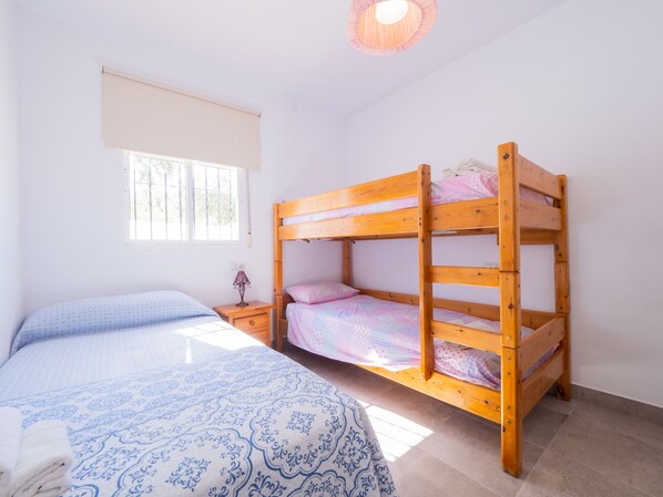 Un dormitorio con una cama individual, una litera y una mesita de noche con lámpara.