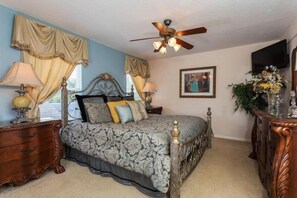 A bedroom with a bed, a ceiling fan, a dresser, a nightstand, a lamp, a framed picture, and a vase with flowers.