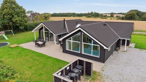 Una casa moderna con un amplio ventanal, un patio con mobiliario exterior y una piscina.