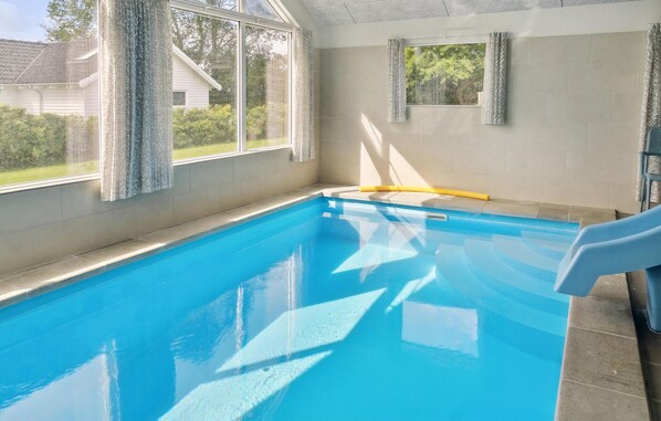 Une piscine intérieure à l’eau d’un bleu limpide, avec un escalier jaune et des fenêtres dotées de rideaux.