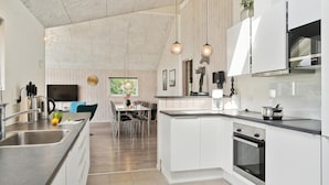 Una cocina moderna con armarios blancos, electrodomésticos de acero inoxidable y un comedor con vistas al verdor.