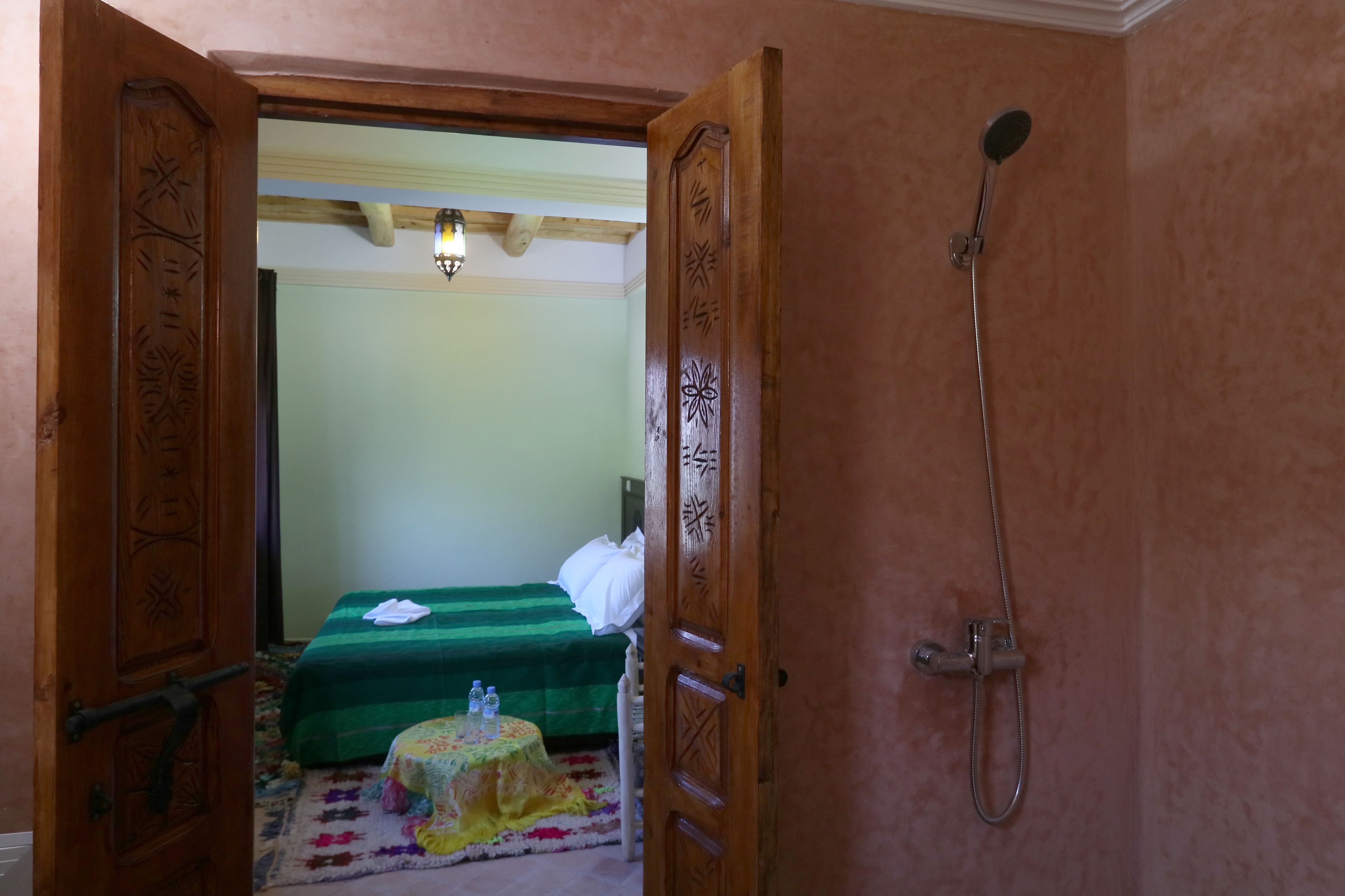 A room with a bed, a small round table with a tablecloth, and a shower.