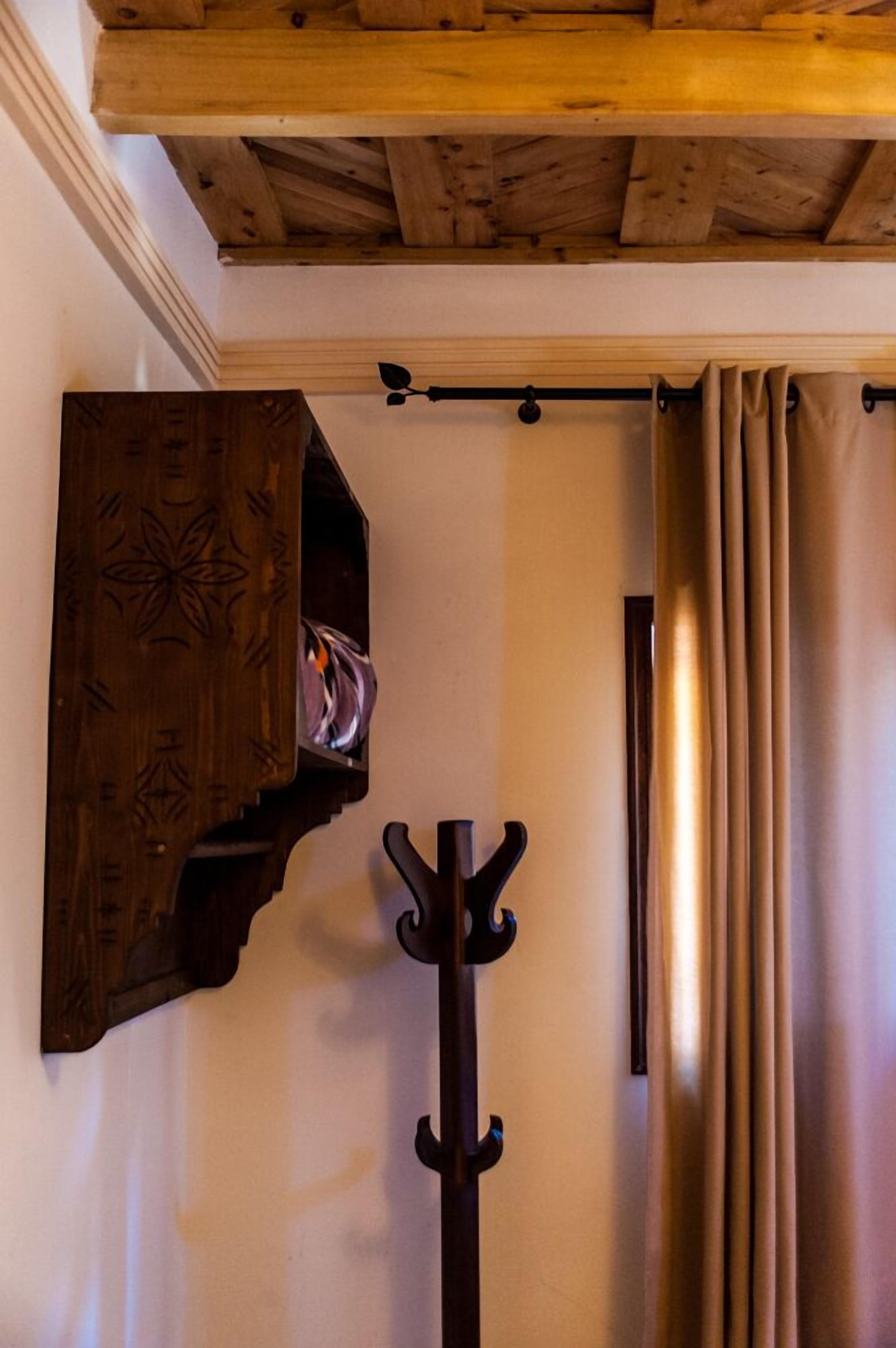 Techo de madera con vigas a la vista, un perchero y un estante de pared con un diseño decorativo.