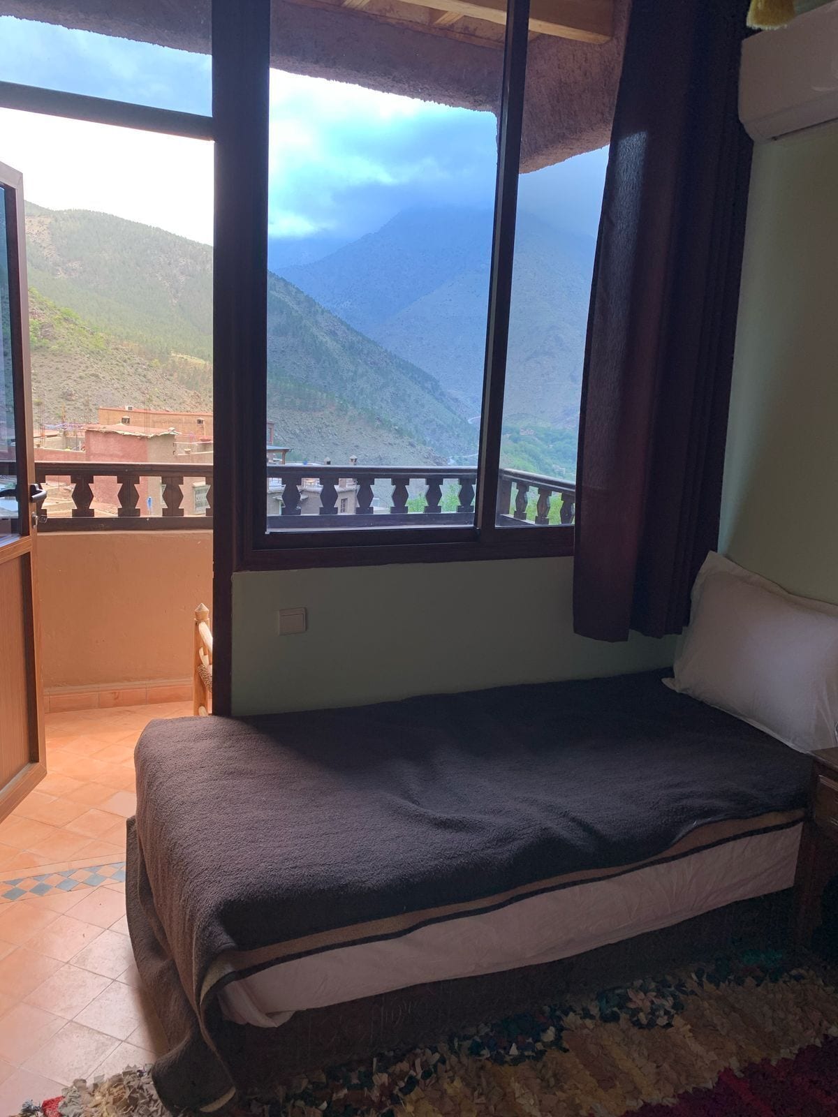 A bedroom with a bed, a window with a view of mountains, and a balcony.