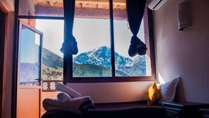 A bedroom with a bed, a window with a view of mountains, a towel on the bed, and a pillow. - Dar Atlas Charme (Asni)