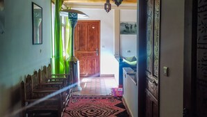 A hallway with a patterned rug, wooden benches, a green curtain, and a wooden door with a heart decoration. - Dar Atlas Charme (Asni)