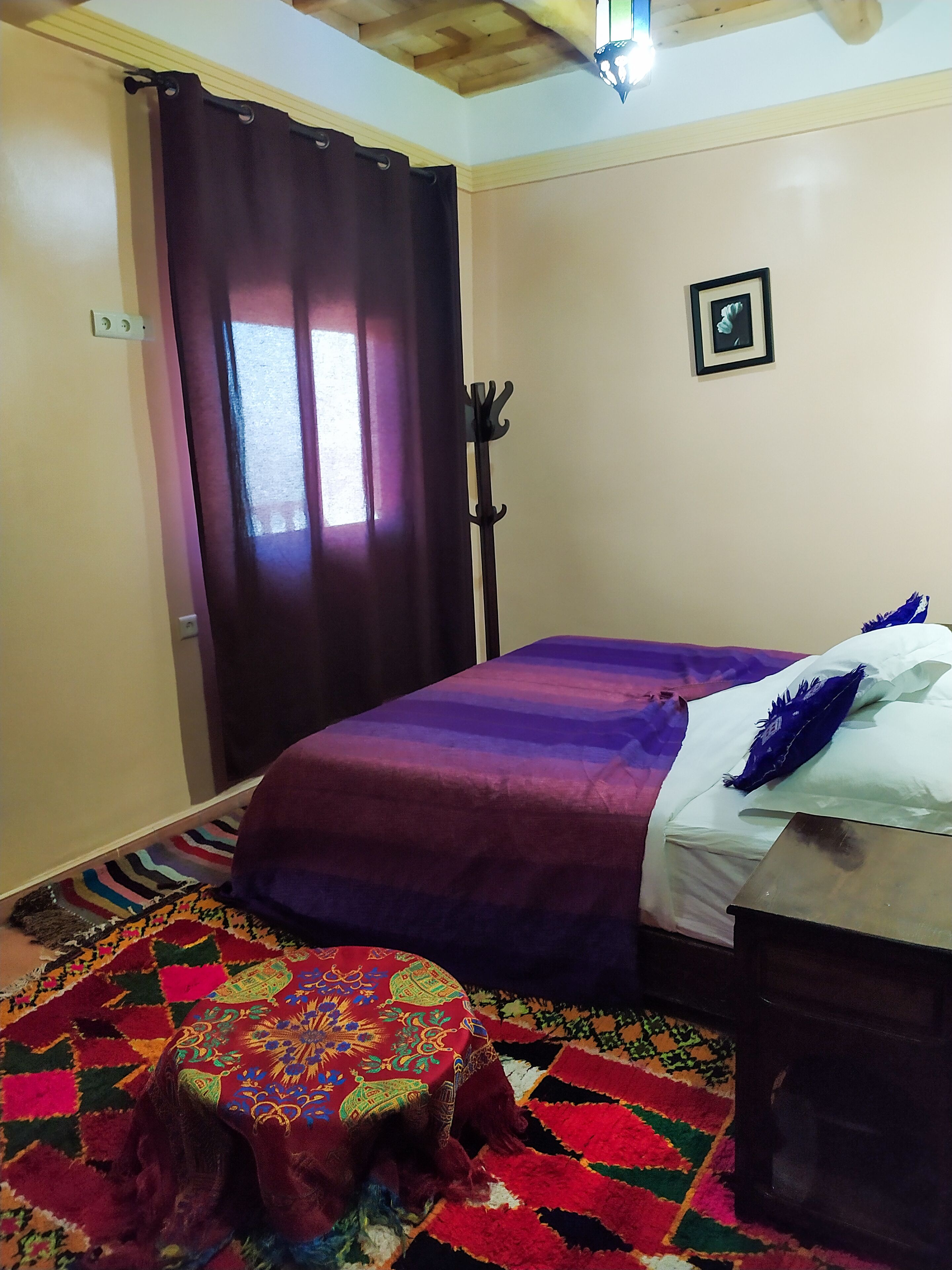 A room with a bed, a small stool, a coat rack, and a picture on the wall.