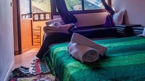 A room with a bed, a window with curtains, a view of mountains, and an air conditioning unit. - Dar Atlas Charme (Asni)