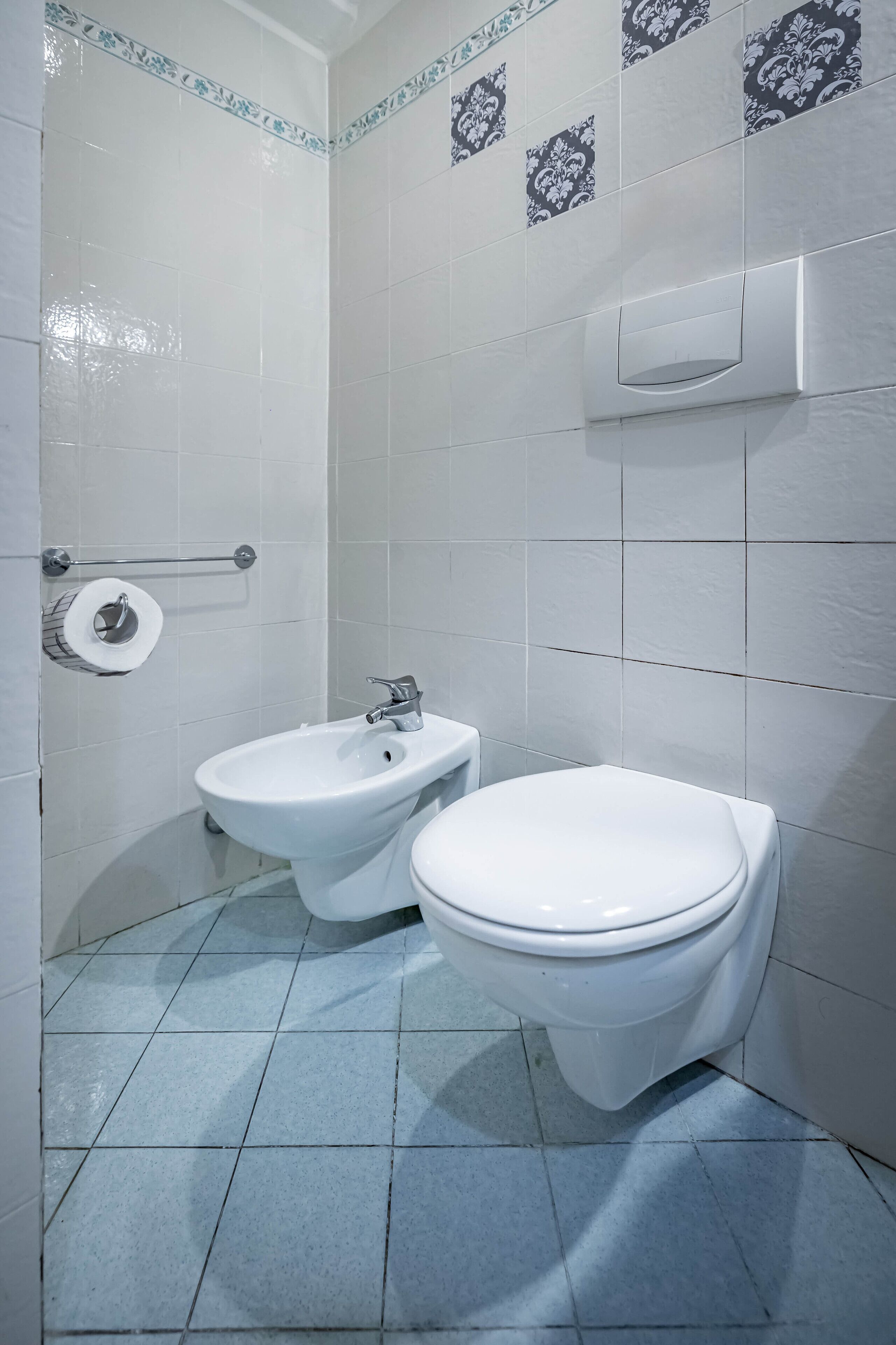 A bathroom with a toilet, bidet, and a toilet paper holder on the wall.