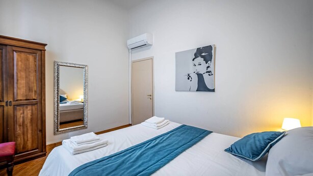 A bedroom with a bed, a mirror, a wardrobe, and a wall-mounted artwork. - Flospirit - Bellini (Florence)