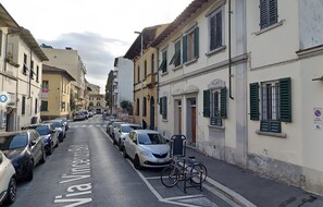 A narrow street lined with parked cars and buildings with green shutters. - Flospirit - Bellini (Florence)