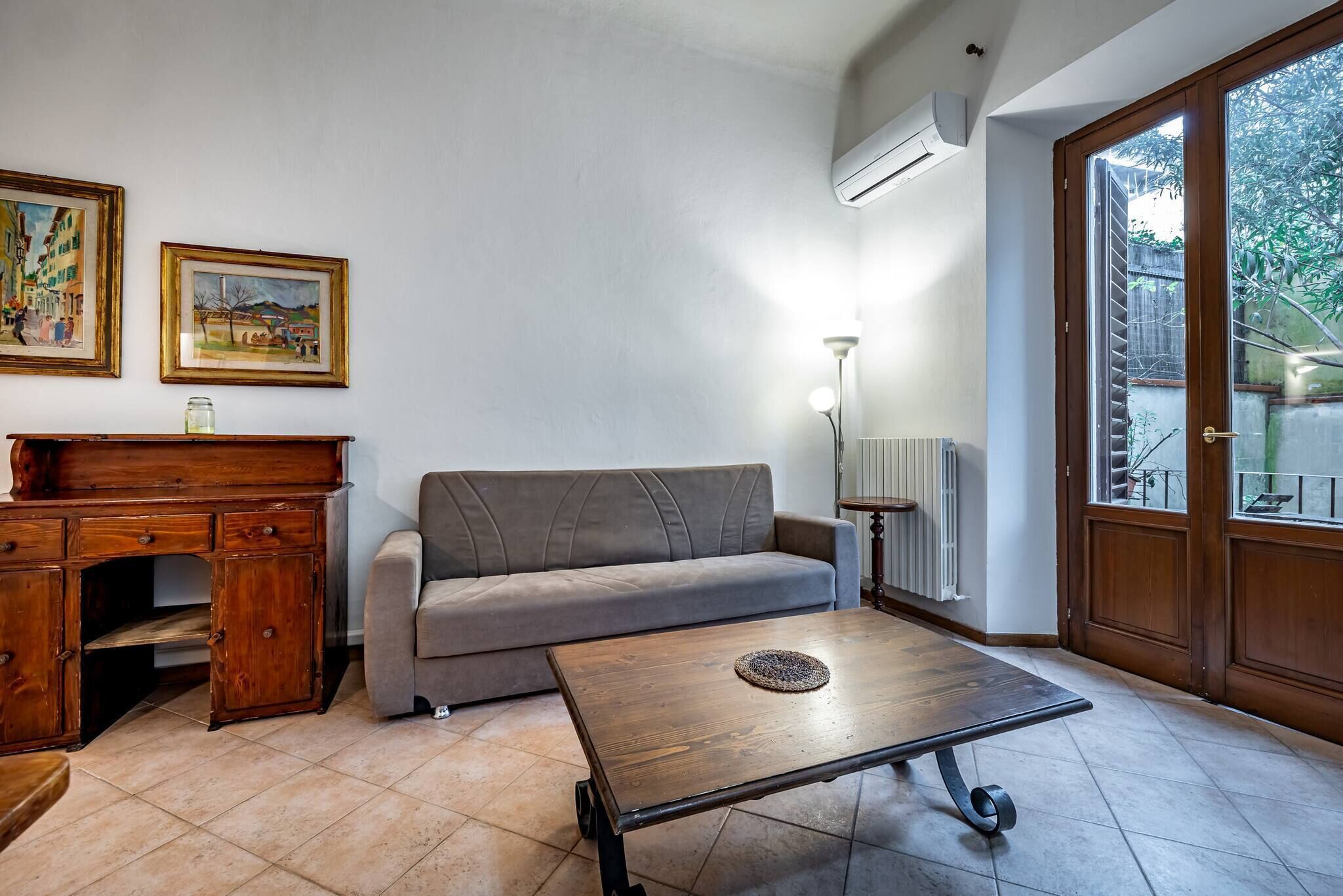 Uma sala de estar com um sofá, uma mesa de centro, uma escrivaninha de madeira e duas fotografias emolduradas na parede.