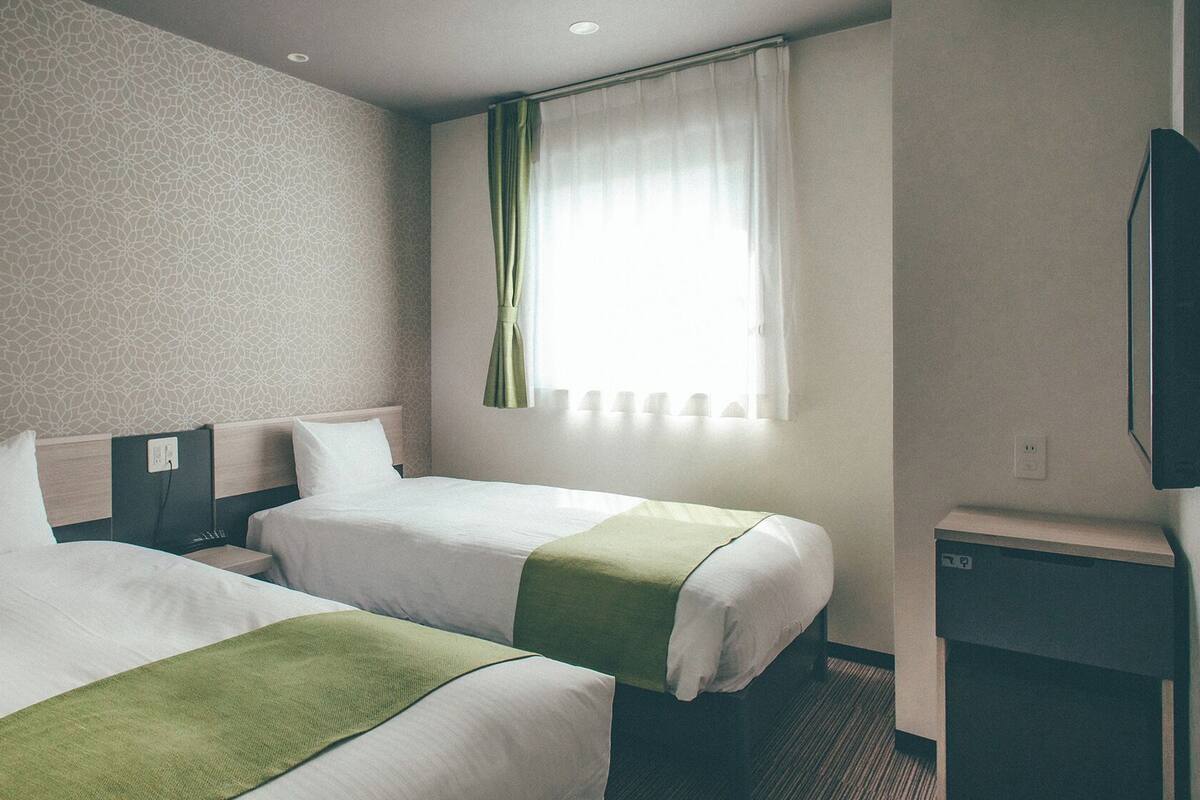 Une chambre d’hôtel avec deux lits, une télévision, une fenêtre avec des rideaux et un mur décoré de motifs.