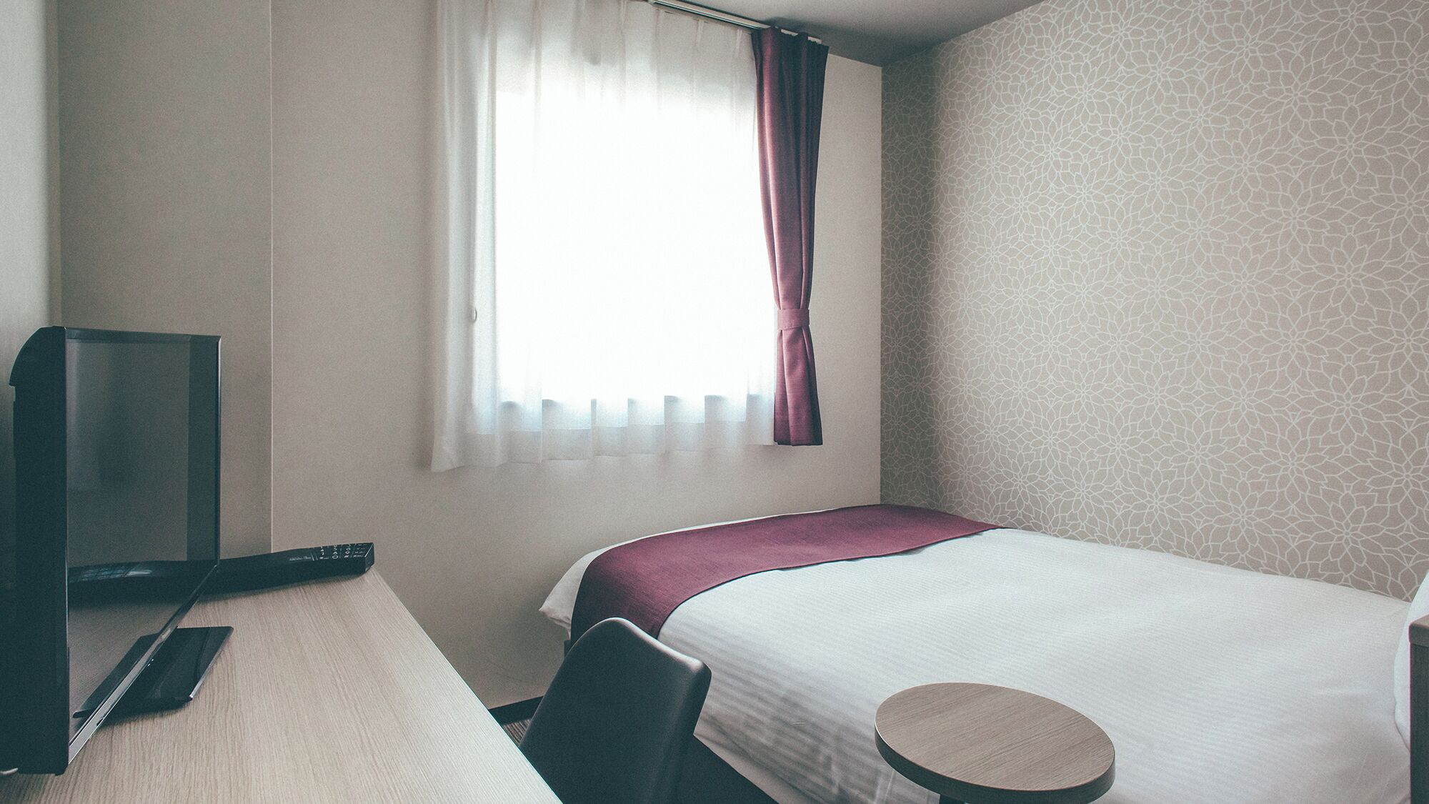 A hotel room with a bed, a desk, a television, and a window with curtains.