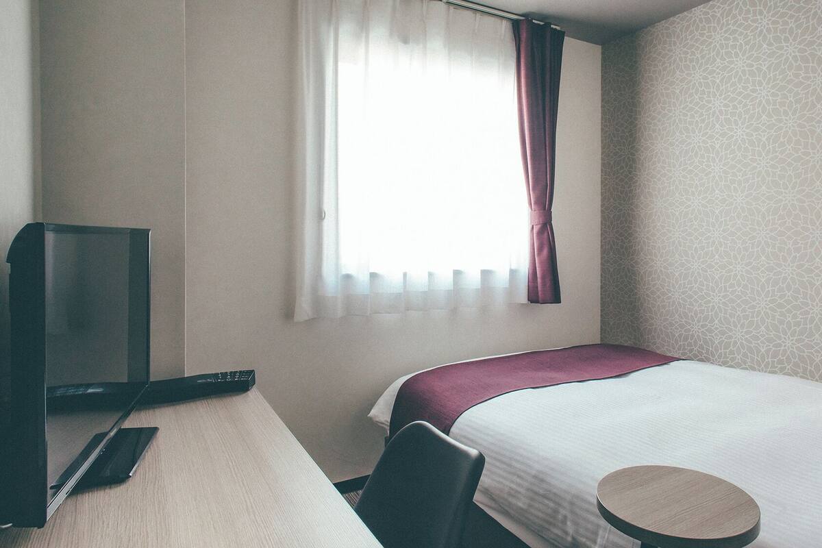 Une chambre d’hôtel avec un lit, un bureau, une télévision et une fenêtre avec des rideaux.
