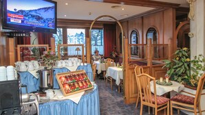 Un comedor de hotel con una televisión mostrando una vista panorámica, una estación de café y una mesa de buffet con alimentos.