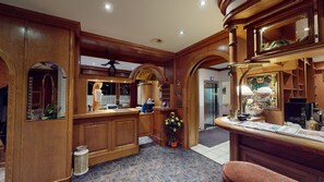 A reception area with wooden paneling, a reception desk, a mirror, a flower arrangement, and an elevator.