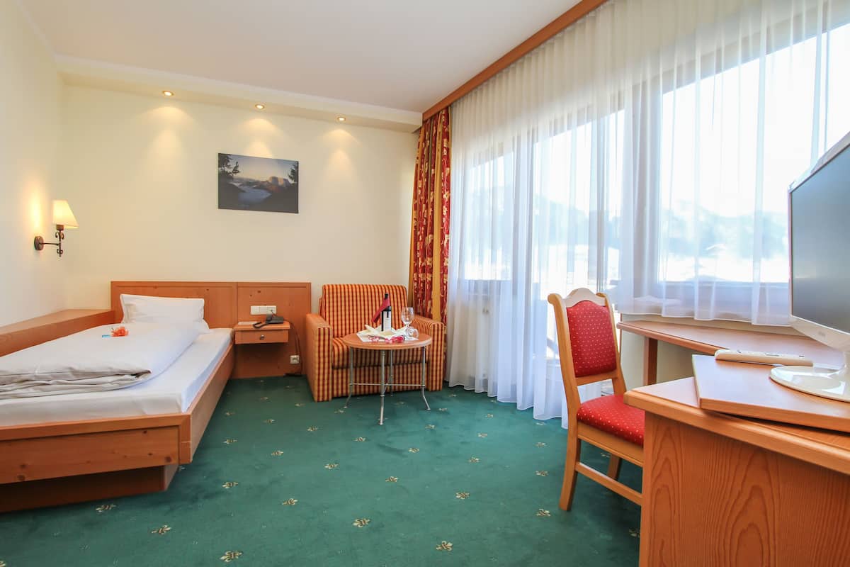 A hotel room with a bed, a desk with a chair, a small table with a lamp, and a TV.