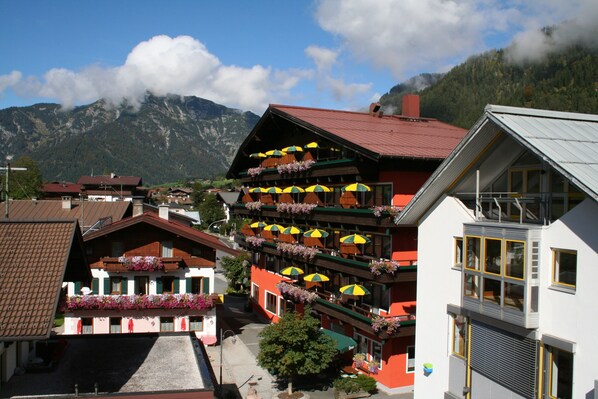 A multi-story building with balconies adorned with flowers and yellow umbrellas, set against a mountainous backdrop. - Hotel Tiroler ADLER Bed & Breakfast (Waidring)