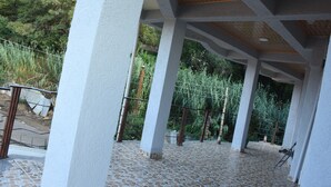 Un espacio exterior techado con suelo de baldosas, columnas y barandilla de metal.