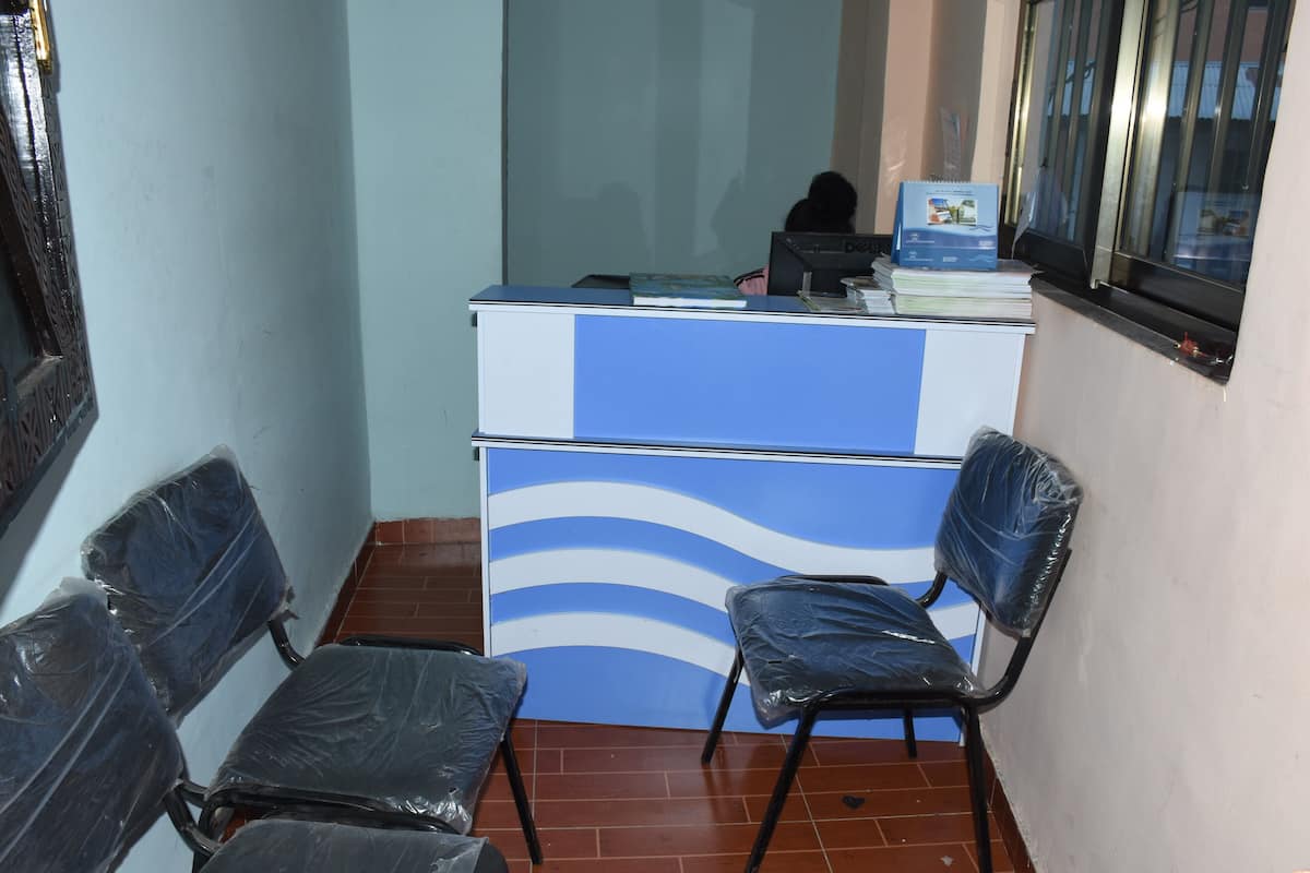 Un mostrador de recepción con una computadora, un diseño de pared azul y blanco, y sillas con fundas de plástico.