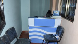 Un mostrador de recepción con una computadora, un diseño de pared azul y blanco, y sillas con fundas de plástico.