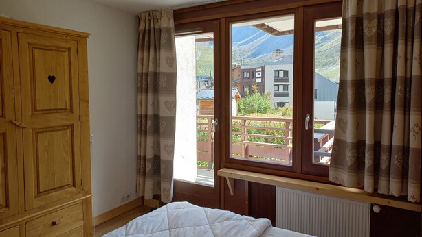 A bedroom with a bed, wooden wardrobe, and a window with curtains.