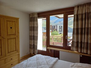 A bedroom with a bed, wooden wardrobe, and a window with curtains.
