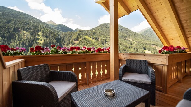 A wooden deck with wicker furniture and a flower border, overlooking a mountainous landscape.