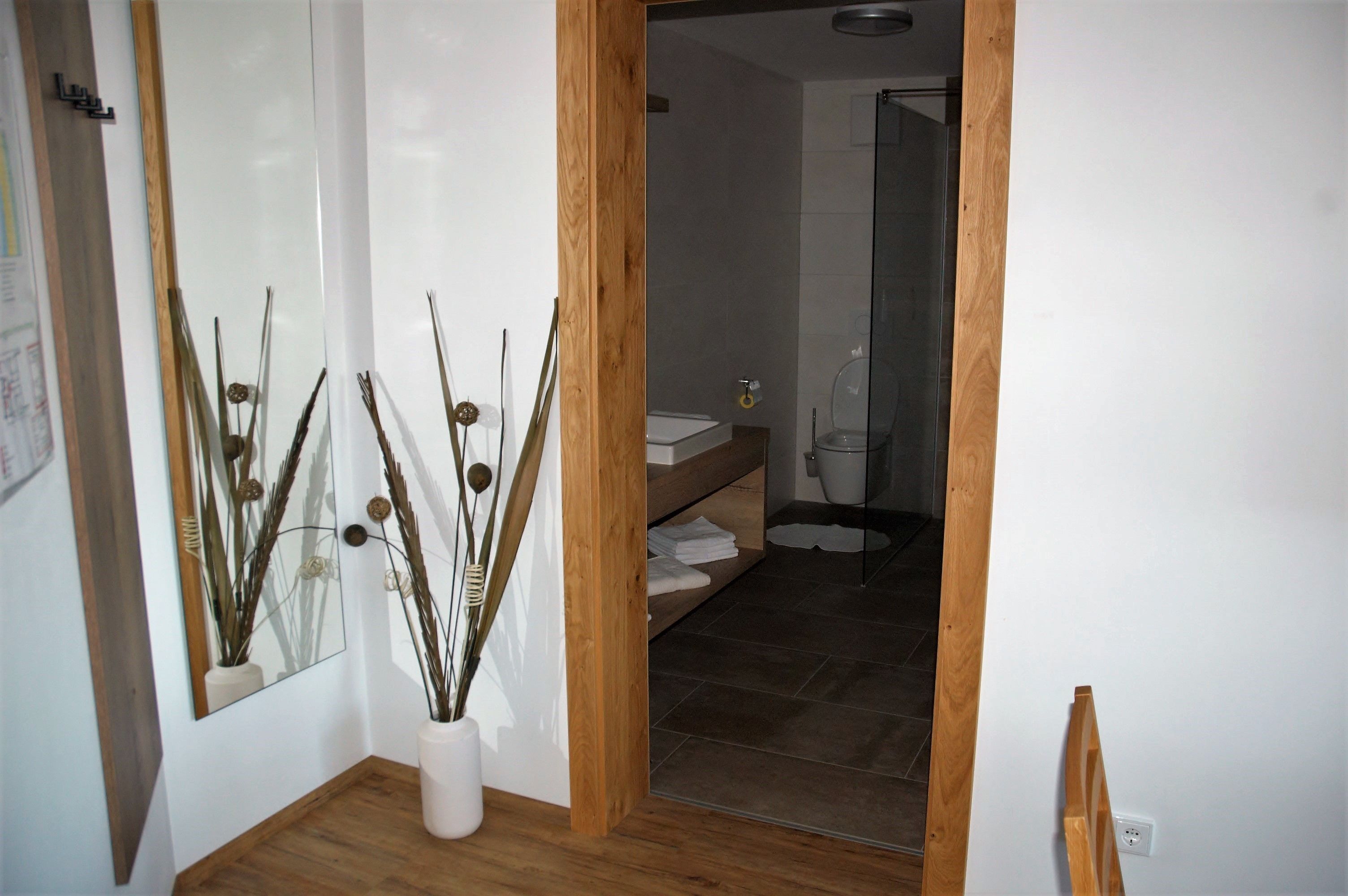A hallway with a mirror, a wooden floor, and a bathroom visible through an open door.