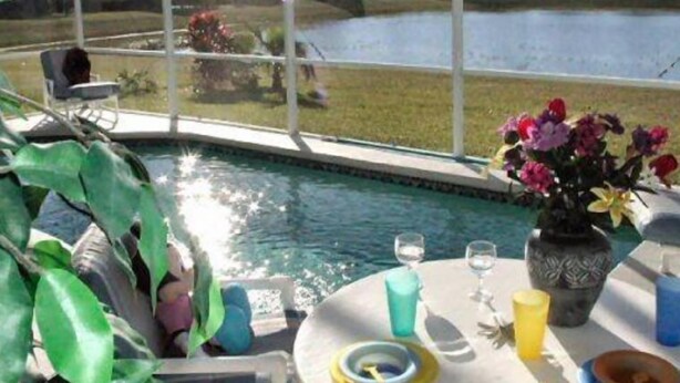 Un espace aménagé au bord de la piscine, avec une table dressée pour deux personnes, un vase rempli de fleurs et une vue sur une vaste étendue d’eau.