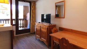 A small room with a wooden table and chairs, a television on a wooden cabinet, a sliding glass door leading to an outdoor area, and a mirror on the wall.