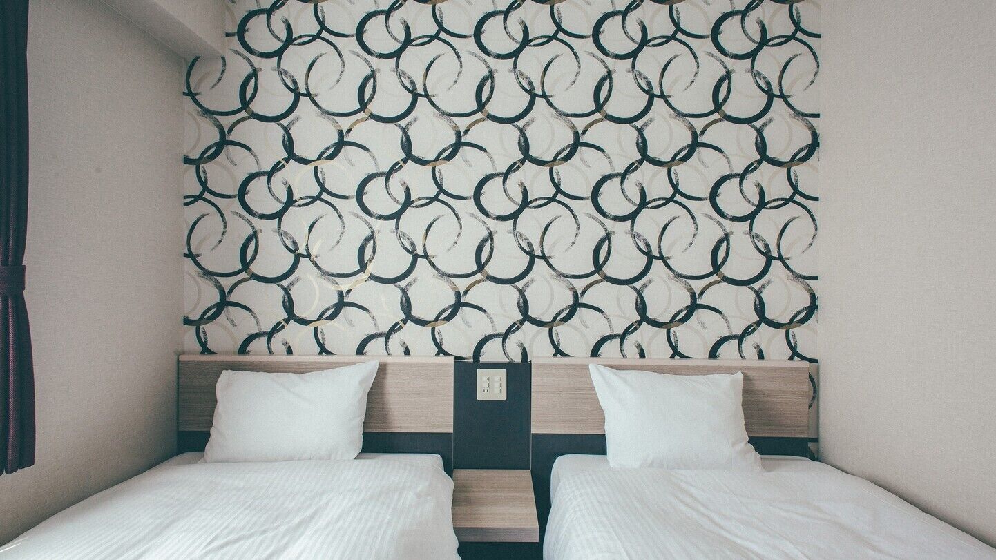 Habitación de hotel con dos camas, un papel tapiz estampado y un cabecero de madera.