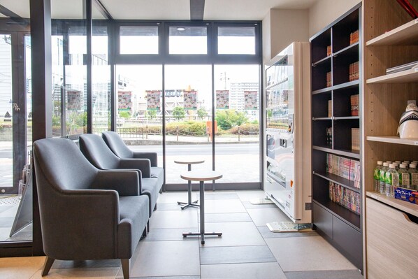 A modern interior with seating, a vending machine, and a view of the outside. - Kuretake Inn Nankai Sakaiekimae (Sakai)