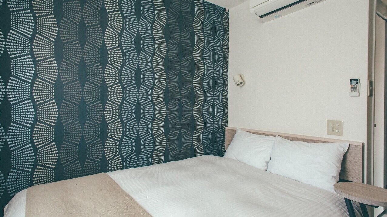Una habitación de hotel con cama, cabecera, teléfono en la pared y toma de corriente.