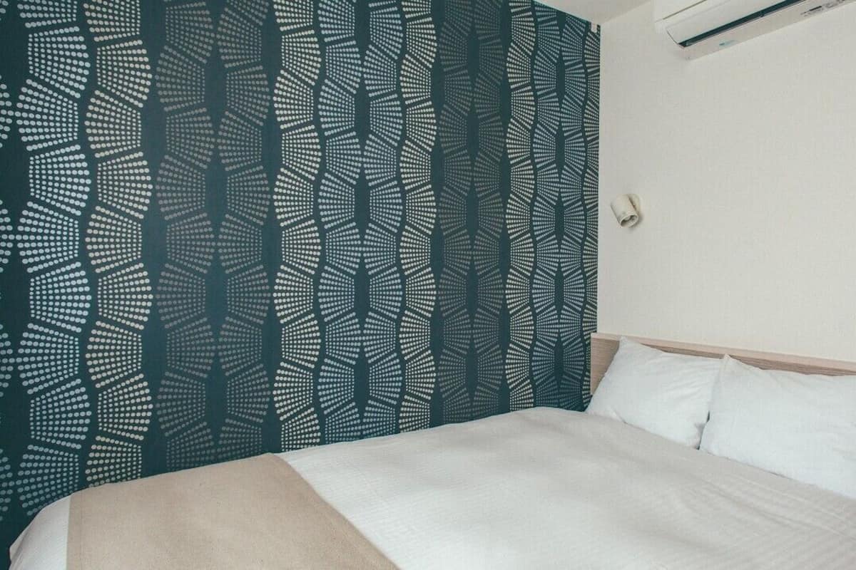 A hotel room with a bed, a headboard, a wall-mounted phone, and a power outlet.