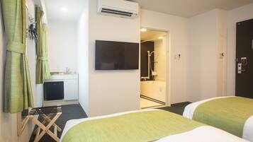 A hotel room with two beds, a TV, an air conditioner, a small kitchenette, and a shower area.