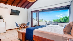 Une chambre avec un grand lit, un bureau et une chaise. Une porte coulissante donne sur l’extérieur et offre une vue sur le paysage.