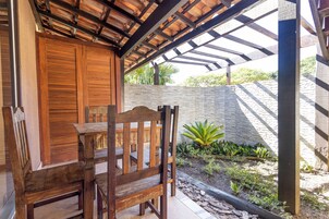 Una mesa y sillas de madera bajo una pérgola, con un muro de piedra y plantas al fondo.