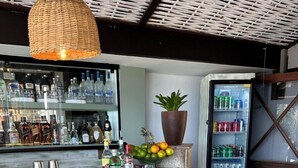 Un espace bar avec des chaises en bois, un comptoir avec des bouteilles, une plante en pot et un réfrigérateur pour les boissons.