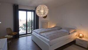 Un dormitorio con cama, mesita de noche, lámpara, silla y vistas amplias a través de un gran ventanal.