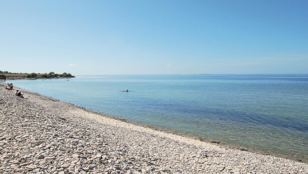 A pebbled beach with clear water and a distant shoreline.