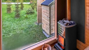 A cozy room with a fireplace, a window overlooking a grassy garden, and a small wooden structure outside.