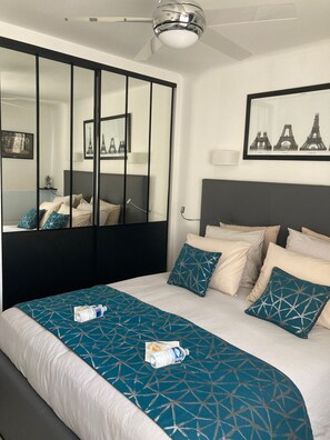 A hotel room with a bed, a large mirror, a ceiling fan, and a framed picture of the Eiffel Tower. - Cannes City B&B (Cannes)