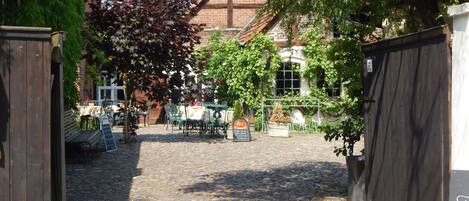 A cobblestone pathway leading to a courtyard with outdoor seating and a brick building.
